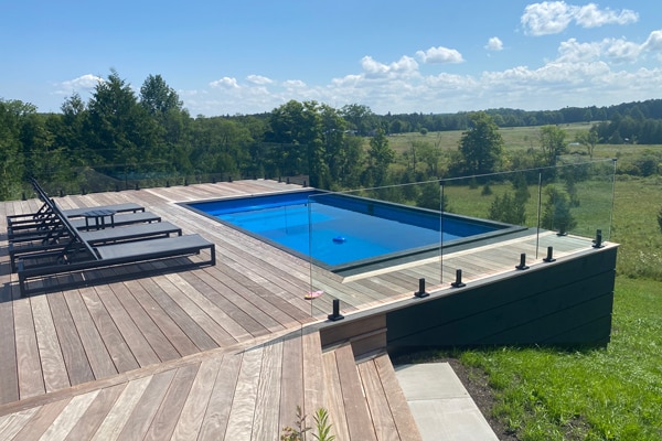 shipping container pool installed on a hill on a sloped property with a deck around it overlooking a large field
