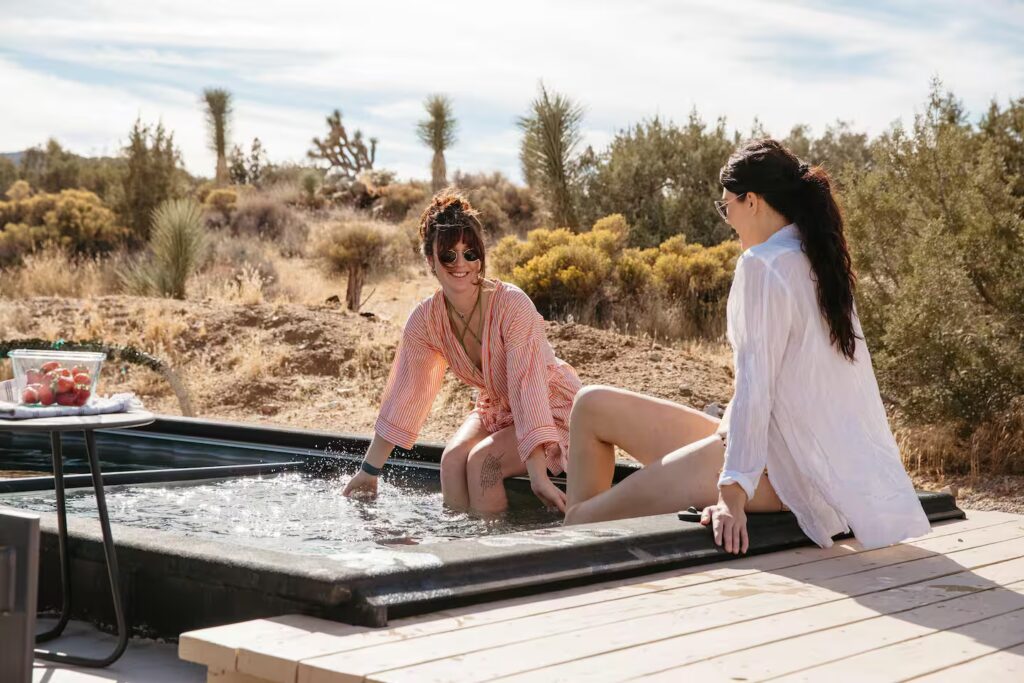 2 female Airbnb guests sitting pool side with their feet in a Modpool container pool.