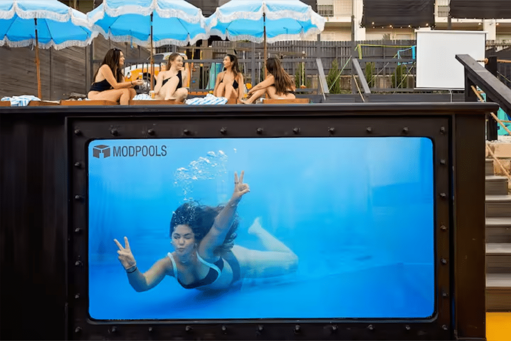 Female Airbnb guest posing for a Instagram photo underwater giving the peace sign through a clear viewing window on the side of the Modpool shipping container pool